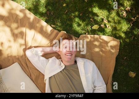 Vue en angle élevé d'un jeune homme joyeux reposant sur une natte dans le parc Banque D'Images