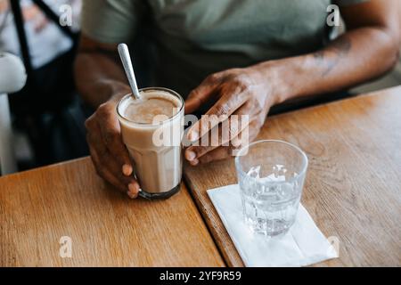 Section médiane de l'homme tenant un verre de café glacé sur la table Banque D'Images