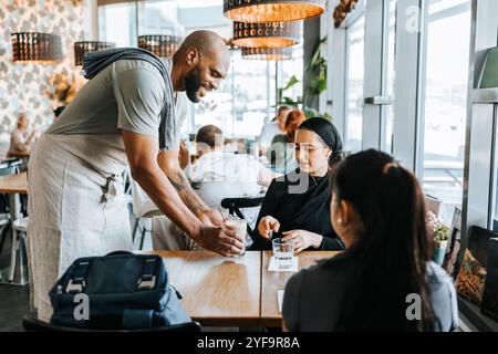 Barista souriant servant du café aux clientes du café Banque D'Images