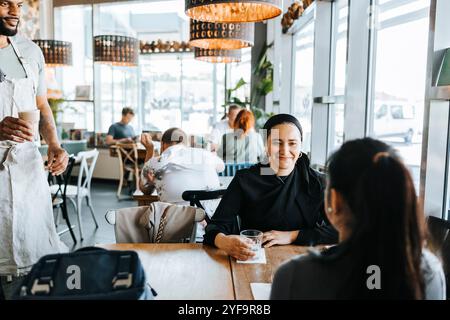 Amies féminines assises pendant que le barista leur sert du café dans un café Banque D'Images
