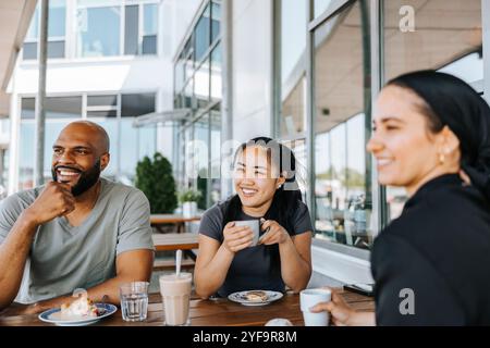 Amis joyeux prenant le petit déjeuner dans le café Banque D'Images