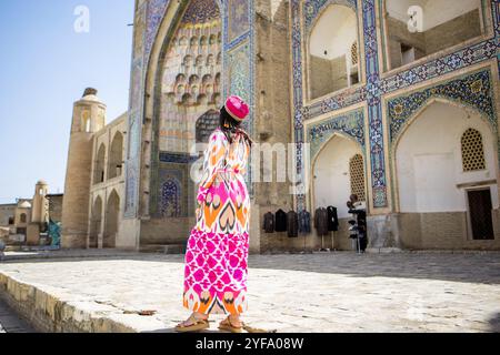 Vue arrière de la jeune femme debout devant la Madrasah dans le centre historique Boukhara, Ouzbékistan Banque D'Images