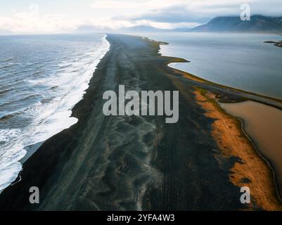 Vue aérienne de la superbe plage de sable noir d'Islande avec les vagues de l'océan qui s'écrasent d'un côté et un lagon serein de l'autre, mettant en valeur le spectaculaire Banque D'Images