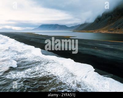 Vue aérienne de la superbe plage de sable noir d'Islande avec les vagues de l'océan qui s'écrasent d'un côté et un lagon serein de l'autre, mettant en valeur le spectaculaire Banque D'Images