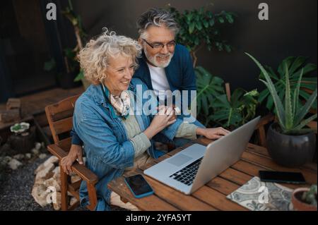 Couple mûr avec ordinateur portable assis dans le jardin. Banque D'Images