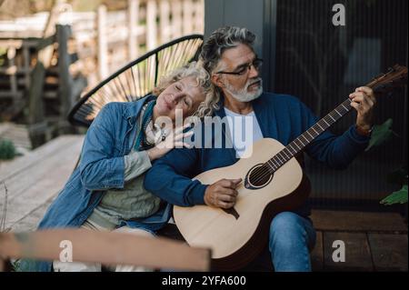 Femme blonde appréciant la guitare de son mari jouant dans le jardin. Banque D'Images