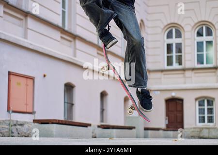 Skateboarder faisant ollie Trick dans Urban Street. Gros plan du patineur portant un Jean baggy en équilibre sur le skateboard. Concept de sous-culture de la jeunesse Banque D'Images