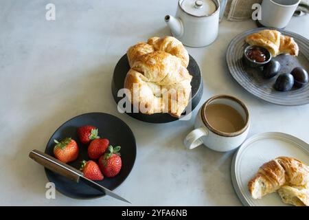 Table de petit déjeuner avec croissants, café, fraises et prunes Banque D'Images