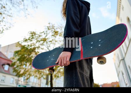 Skateboarder dans un Jean baggy tenant un skateboard rose rayé dans la rue de la ville. Adolescent fait du skateboard. Concept de sous-culture de la jeunesse Banque D'Images