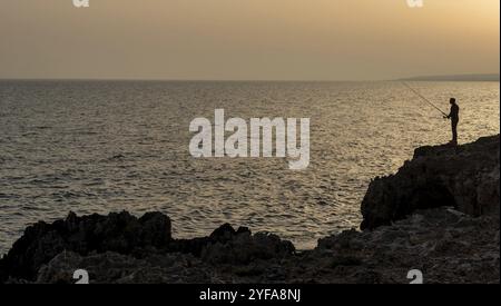 Silhouette d'un pêcheur pêcheur pêchant dans l'océan au coucher du soleil. Ayia Napa, Chypre, Europe Banque D'Images