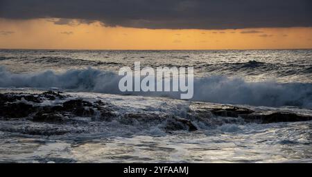 Des vagues venteuses éclaboussant sur la côte rocheuse au coucher du soleil. Ciel orageux en hiver à l'océan Banque D'Images