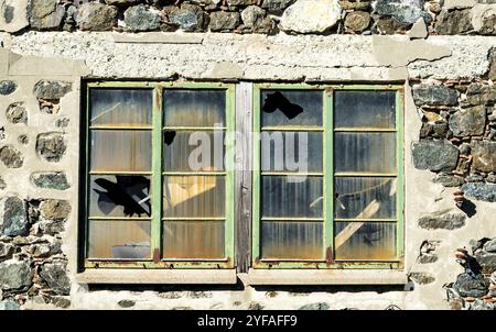 Fenêtres métalliques fermées sur un mur dénoyauté avec du verre brisé d'un bâtiment abandonné Banque D'Images