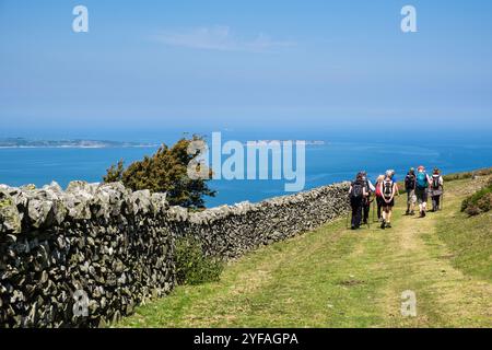 Groupe de marcheurs marchant le long d'un mur de pierre sèche avec vue sur le détroit de Menai d'au-dessus de Llanfairfechan, Conwy, pays de Galles, Royaume-Uni, Grande-Bretagne, Europe Banque D'Images