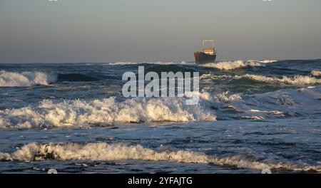 Navire abandonné dans la mer orageuse avec de grandes vagues de vent au coucher du soleil. Naufrage dans l'océan Banque D'Images