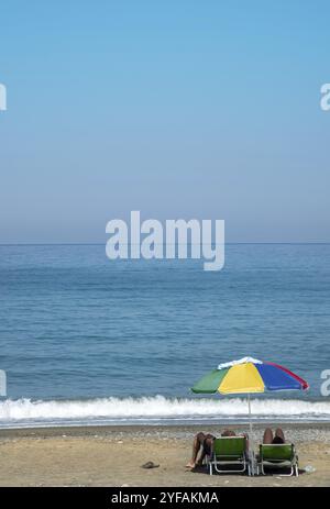 Les gens méconnus assis sous le parasol profitant de la mer calme à la plage pendant les vacances d'été Banque D'Images