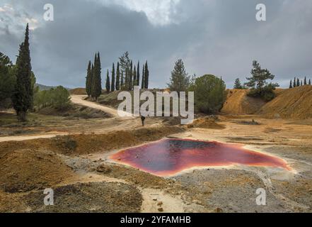 Méconnaissable man walking sur près d'un lac avec de l'eau toxique polluée rouge une mine de cuivre de la zone Mitsero à Chypre Banque D'Images