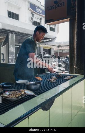 Un chef prépare du poisson grillé commandé par un client dans son restaurant à Palopo City, le 1er octobre 2024, Sulawesi du Sud, Indonésie Banque D'Images