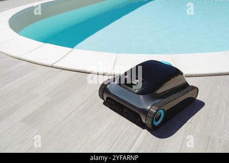 Un robot nettoyeur de piscine devant une piscine extérieure avec de l'eau bleu vif, prêt pour un nettoyage sous-marin efficace et l'enlèvement des débris. Espace pour le texte Banque D'Images