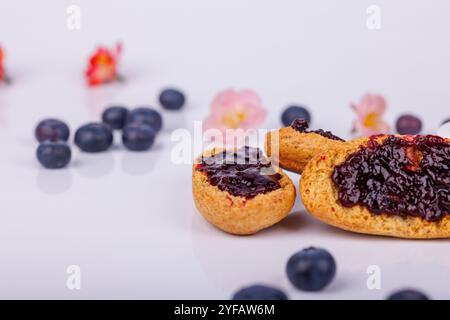 Toast surmonté de confiture de myrtilles fraîches à côté d'un pot, sur un fond blanc, avec des détails riches de couleur et de texture Banque D'Images