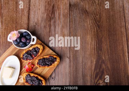 Toast à la confiture de myrtilles se trouve sur une planche à découper en bois, à côté d'un plat de beurre sur une table sombre, créant une scène de petit-déjeuner rustique Banque D'Images