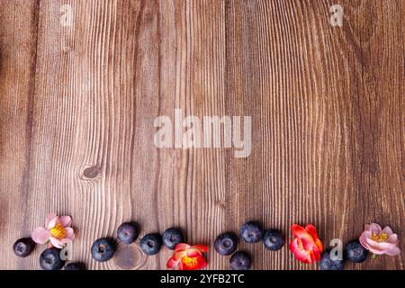 Une photo au-dessus d'une table en bois sombre avec des bleuets frais et des fleurs colorées au fond, créant une scène vibrante et naturelle Banque D'Images