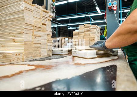 Ouvrier manipulant des piles de planches de bois dans une usine de travail du bois, préparant des matériaux pour un traitement ultérieur sous éclairage industriel Banque D'Images