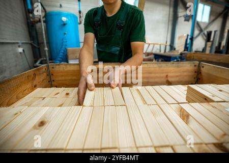 Ouvrier manipulant des piles de planches de bois dans une usine de travail du bois, préparant des matériaux pour un traitement ultérieur sous éclairage industriel Banque D'Images