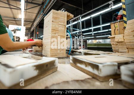 Ouvrier manipulant des piles de planches de bois dans une usine de travail du bois, préparant des matériaux pour un traitement ultérieur sous éclairage industriel Banque D'Images