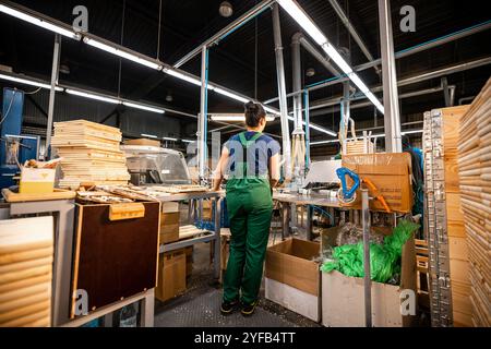 Ouvrier manipulant des piles de planches de bois dans une usine de travail du bois, préparant des matériaux pour un traitement ultérieur sous éclairage industriel Banque D'Images