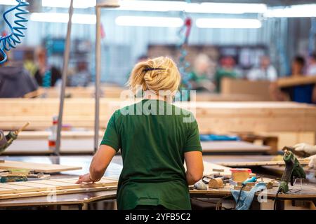 Ouvrier manipulant des piles de planches de bois dans une usine de travail du bois, préparant des matériaux pour un traitement ultérieur sous éclairage industriel Banque D'Images