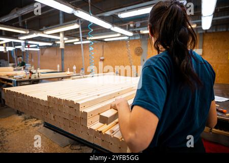 Ouvrier manipulant des piles de planches de bois dans une usine de travail du bois, préparant des matériaux pour un traitement ultérieur sous éclairage industriel Banque D'Images