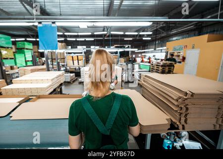 Ouvrier manipulant des piles de planches de bois dans une usine de travail du bois, préparant des matériaux pour un traitement ultérieur sous éclairage industriel Banque D'Images