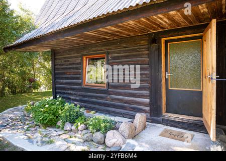 Entrée de cabine rustique avec une porte en bois, un chemin en pierre et un petit jardin, entouré d'une végétation luxuriante. Banque D'Images