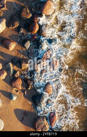 gros plan des vagues qui s'écrasent contre les rochers sur une plage de sable, mettant en valeur la beauté naturelle du littoral. Banque D'Images