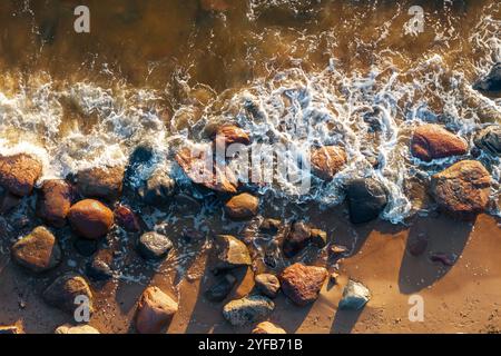 gros plan des vagues qui s'écrasent contre les rochers sur une plage de sable, mettant en valeur la beauté naturelle du littoral. Banque D'Images