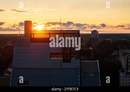 Vue aérienne de Riga au coucher du soleil, avec la rivière Daugava, les ponts et les bâtiments historiques sous un ciel orange chaud. Banque D'Images