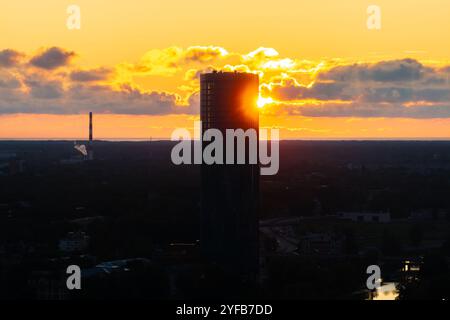 Vue aérienne de Riga au coucher du soleil, avec la rivière Daugava, les ponts et les bâtiments historiques sous un ciel orange chaud. Banque D'Images