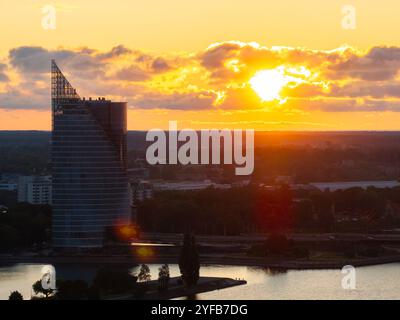 Vue aérienne de Riga au coucher du soleil, avec la rivière Daugava, les ponts et les bâtiments historiques sous un ciel orange chaud. Banque D'Images