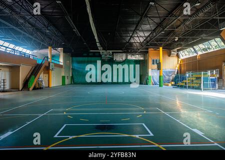 Salle de sport intérieure dotée d'un terrain de basket-ball, de sièges escamotables et de grandes fenêtres offrant une lumière naturelle abondante. Banque D'Images