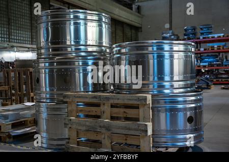 Gros plan de grands cylindres métalliques empilés sur des palettes en bois à l'intérieur d'une usine, mettant l'accent sur leur surface polie et leur cadre industriel. Banque D'Images