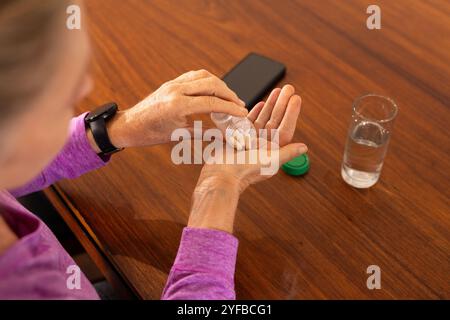 femme âgée prenant des vitamines à la maison avec smartphone et eau sur la table Banque D'Images
