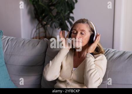 Détente sur le canapé, femme senior profitant de la musique avec des écouteurs à la maison Banque D'Images