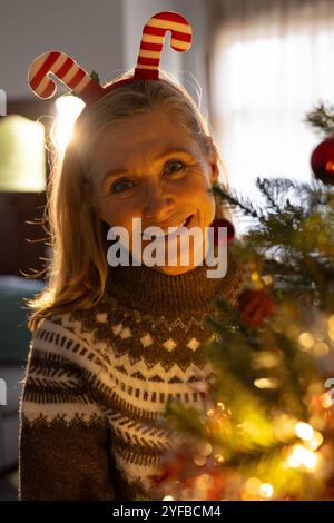 Femme âgée souriante portant bandeau festif décorant l'arbre de Noël à la maison Banque D'Images