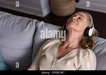Détente sur le canapé, femme senior profitant de la musique avec des écouteurs à la maison Banque D'Images