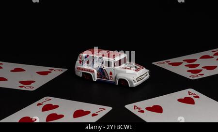 Voiture jouet sur le thème de la Reine de cœur entourée de cartes à jouer sur un fond noir, journée nationale de jeu de cartes Banque D'Images