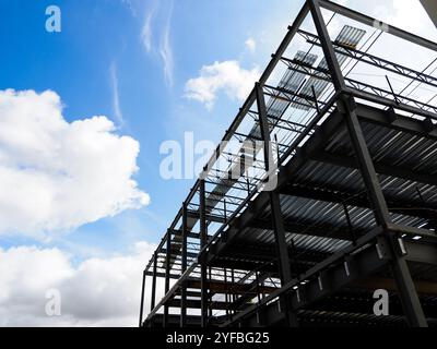 Construction d'une ossature moderne en acier sous un ciel bleu vif avec des nuages moelleux à midi Banque D'Images