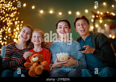 Joyeux Noël et Bonne Année.Les gens s'amusent près de l'arbre à l'intérieur.Toute la famille aime regarder des films de vacances à la maison.Mère, père et filles Banque D'Images