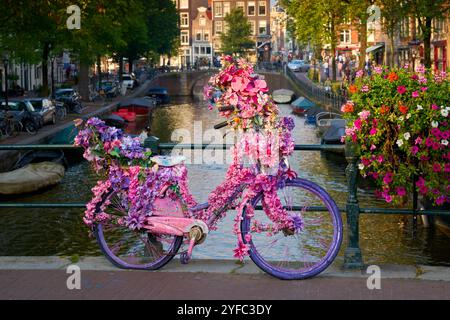 Vélo vintage décoré de fleurs Amsterdam. Vieux vélo vintage décoré de fleurs roses appuyées sur la balustrade d'un pont de canal. Amsterdam, Nethe Banque D'Images