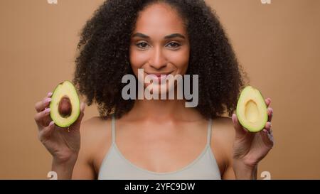 Portrait afro-américain belle femme souriante fille femelle avec cheveux bouclés beauté de soins de la peau saine au fond beige studio tenant deux demi Banque D'Images