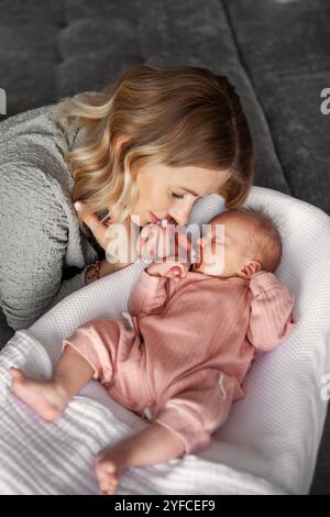 Belle mère regarde avec amour le bébé nouveau-né endormi, habillé en onesie rose et a sucette dans la bouche. Moment serein à la maison, reflète un lien profond Banque D'Images